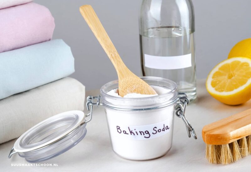 vlekken uit kleding met baking soda: een houten lepel in een pot met baking soda en een stapel wasgoed ernaast | biologisch afbreekbaar