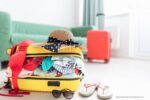 huis oprumen voor vakantie: een overvolle koffer met een hoed erop en slippers ernaast