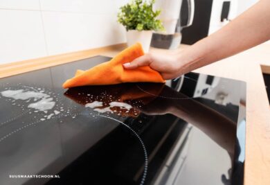 Inductiekookplaat schoonmaken: een hand met een doek die een inductiekookplaat schoonmaakt