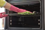 oven schoonmaken: hand met huishoudhandschoenen maakt oven schoon