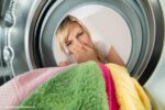 weer in kleding: een vrouw kijkt in de wasmachine en knijpt haar neus dicht