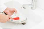 witte sneakers schoonmaken: een persoon die een sneaker wast met een borstel