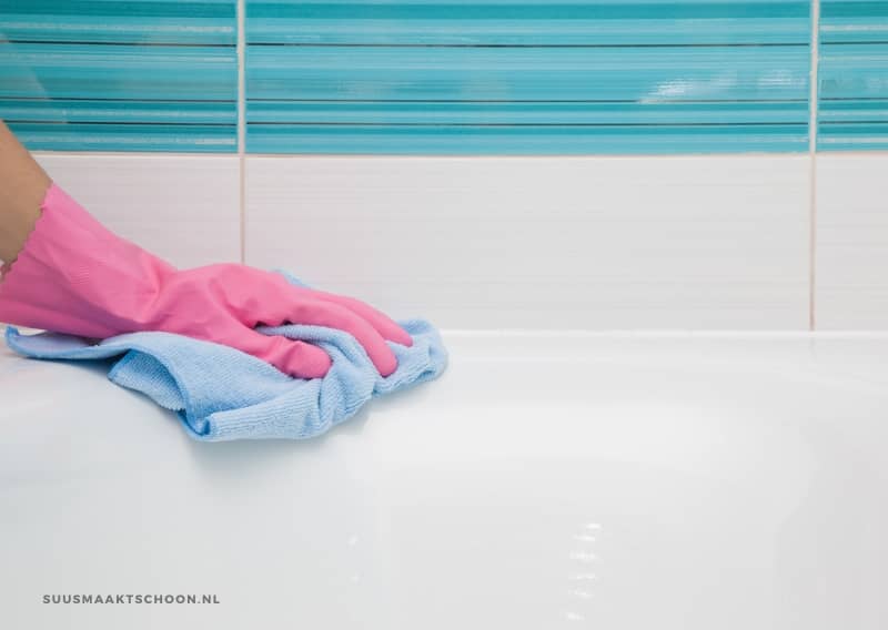 badkamer schoon: een hand in roze huishoudhandschoen veegt badkuip schoon