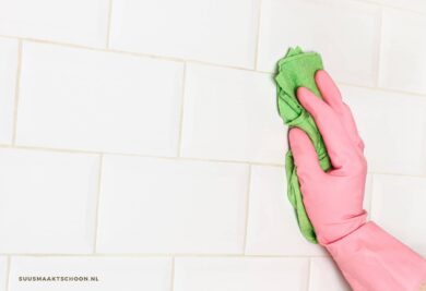 voegen schoonmaken: een hand in roze huishoudhandschoen die een tegelwand schoonmaakt