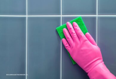 Zeepresten van tegels verwijderen: een hand in een roze handschoen die een tegelwand schoonmaakt