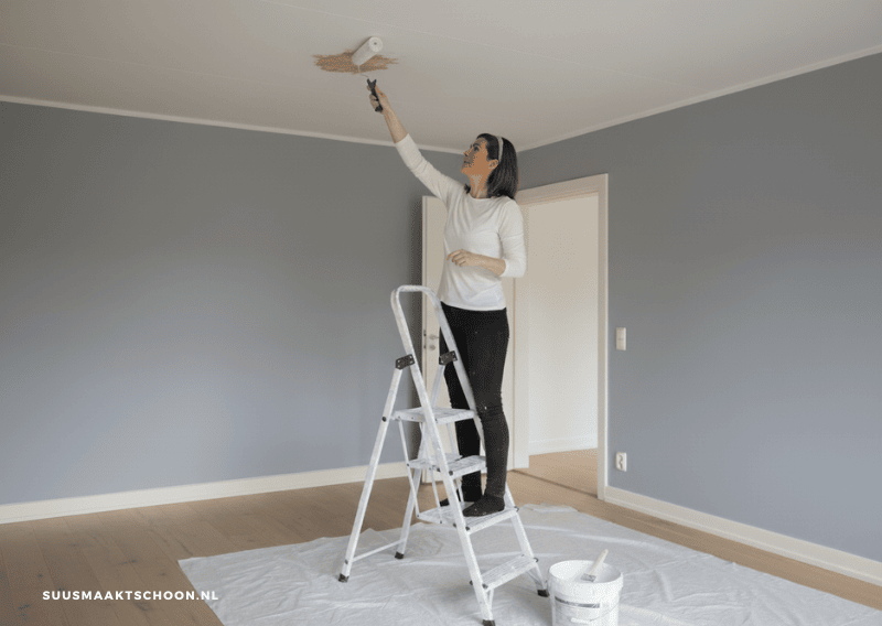Vrouw schildert plafond met roller.