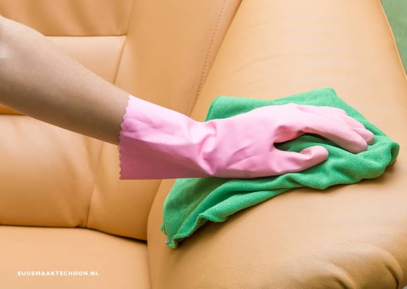 Hand met roze handschoen die leren bank schoonmaken