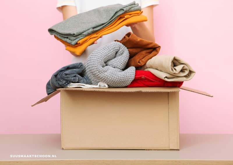 Persoon die opgevouwen kleding in een kartonnen doos legt als onderdeel van Project 333, de minimalistische kledingchallenge waarbij je met 33 items je kast snel opruimt.