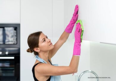 Vrouw met roze schoonmaakhandschoenen die vette keukenkastjes schoonmaakt met een zachte doek in een moderne witte keuken.