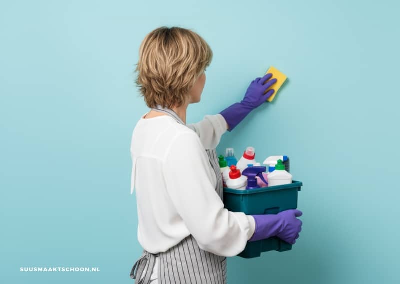 Vrouw maakt vlekken op de muur schoon met spons en schoonmaakmiddel
